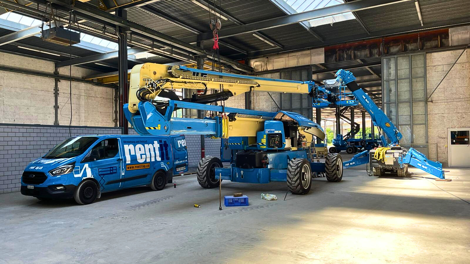 Servicewagen und Gelenkbühne stehen in einer sonnendurchfluteten Halle. Der Hallenkran wird zur Reparatur der Maschine verwendet.